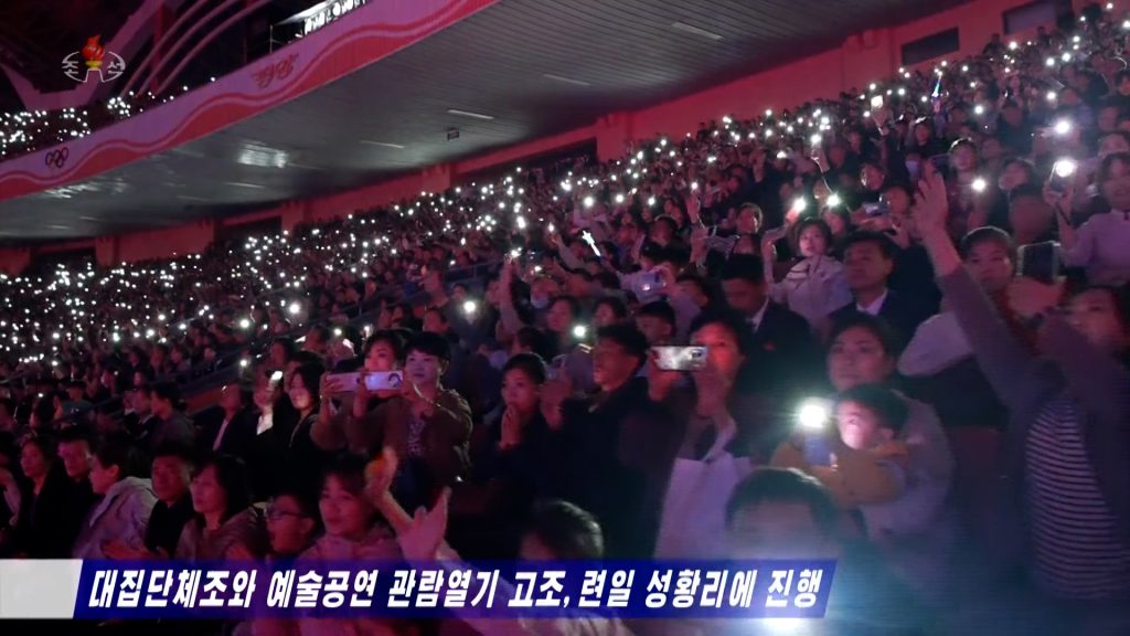 A large crowd of people in a stadium holding their smartphones to film an event, and use their smartphone flashlights