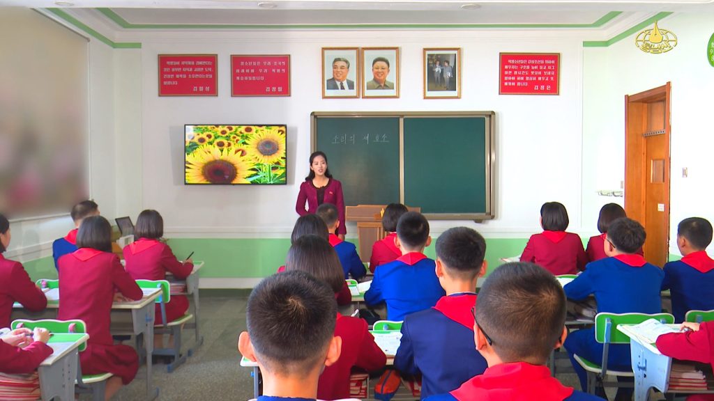The image shows a teacher standing in front of her class